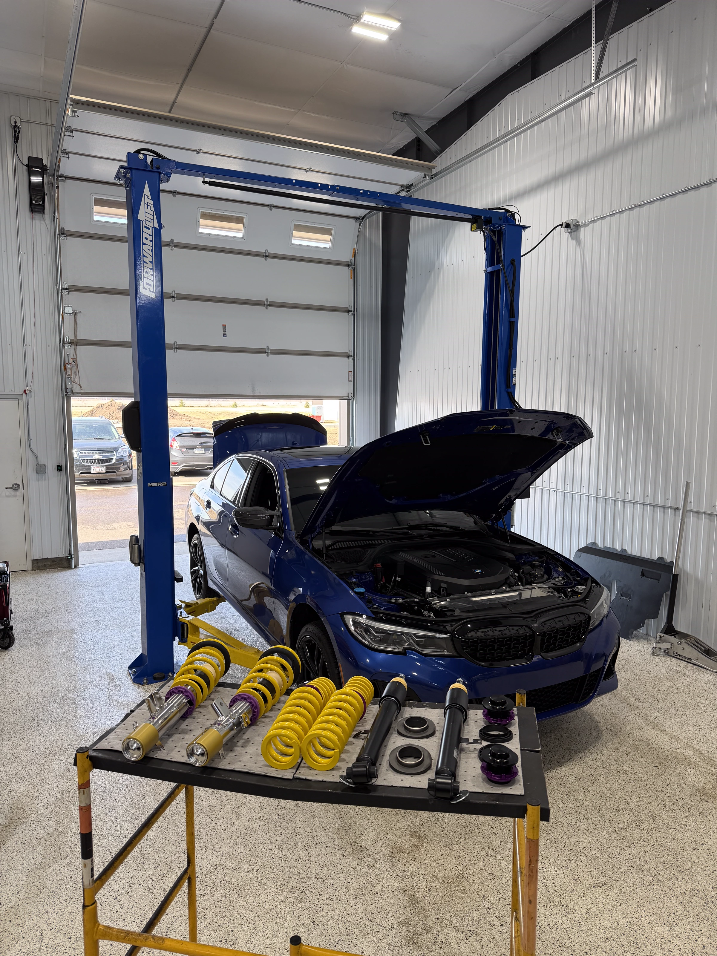Blue BMW 3 Series on the lift with coilovers staged at The Upgrade Shop
