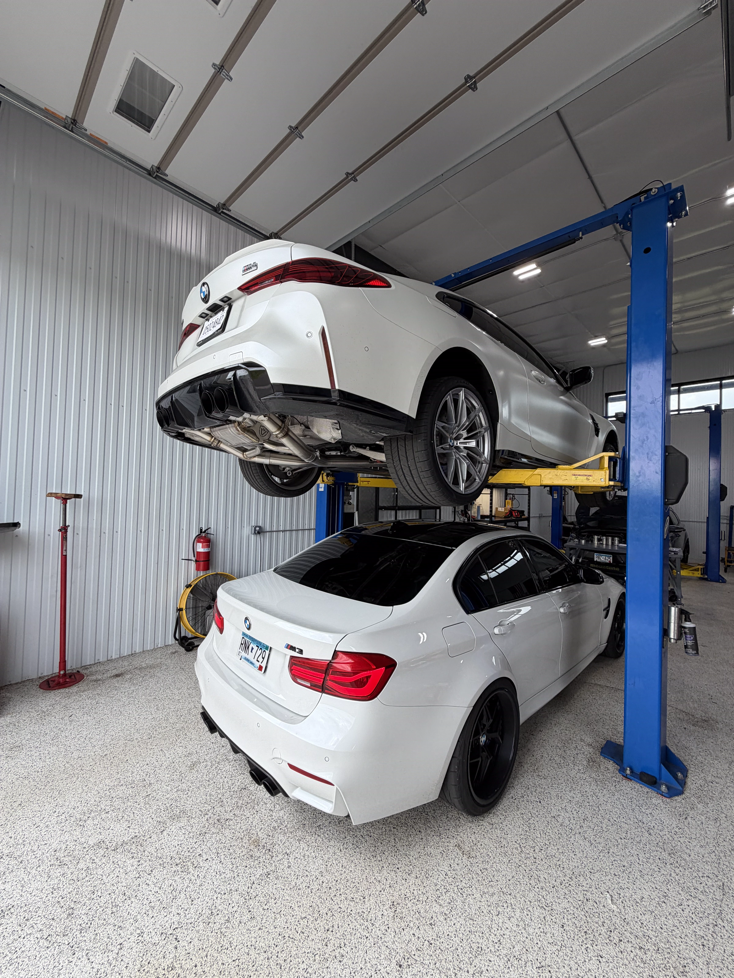 White BMW M4 on the lift and a BMW M3 in the bay at The Upgrade Shop